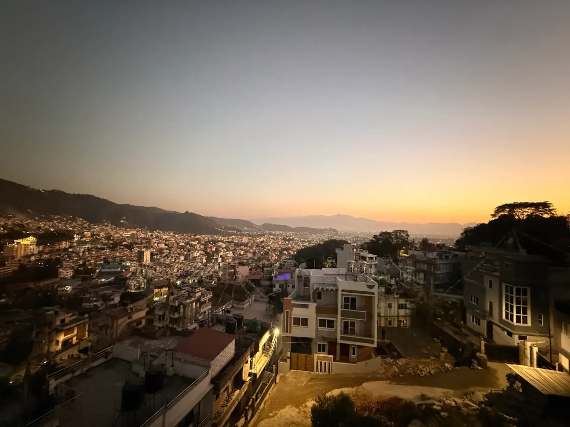 Golden-hour view across Budhanilkantha rooftops towards the Kathmandu Valley