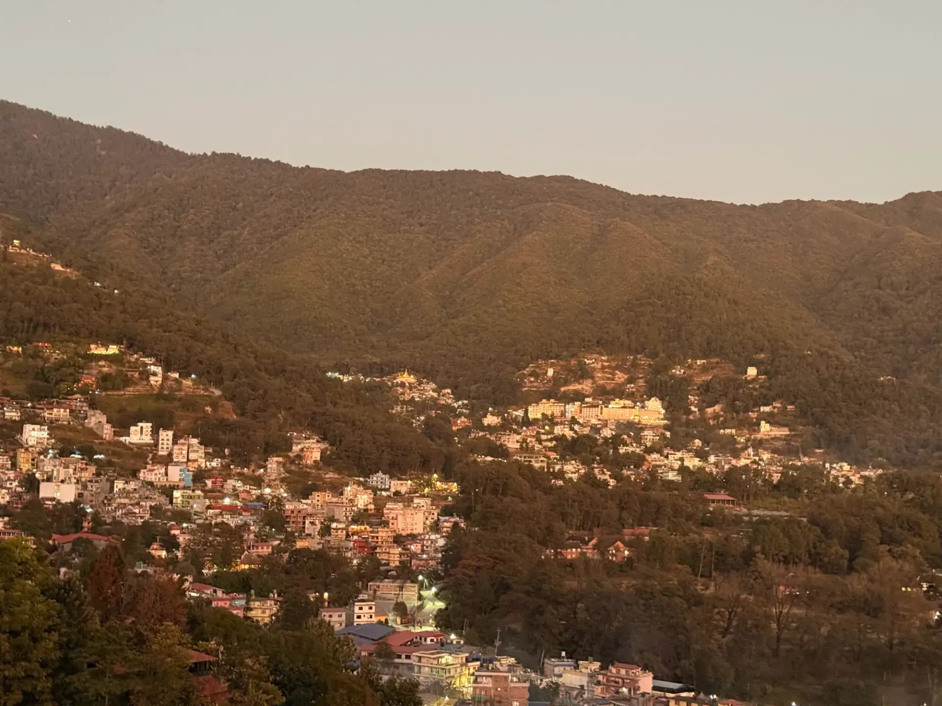 Forested Shivapuri hills and hillside homes at dusk, seen from the homestay