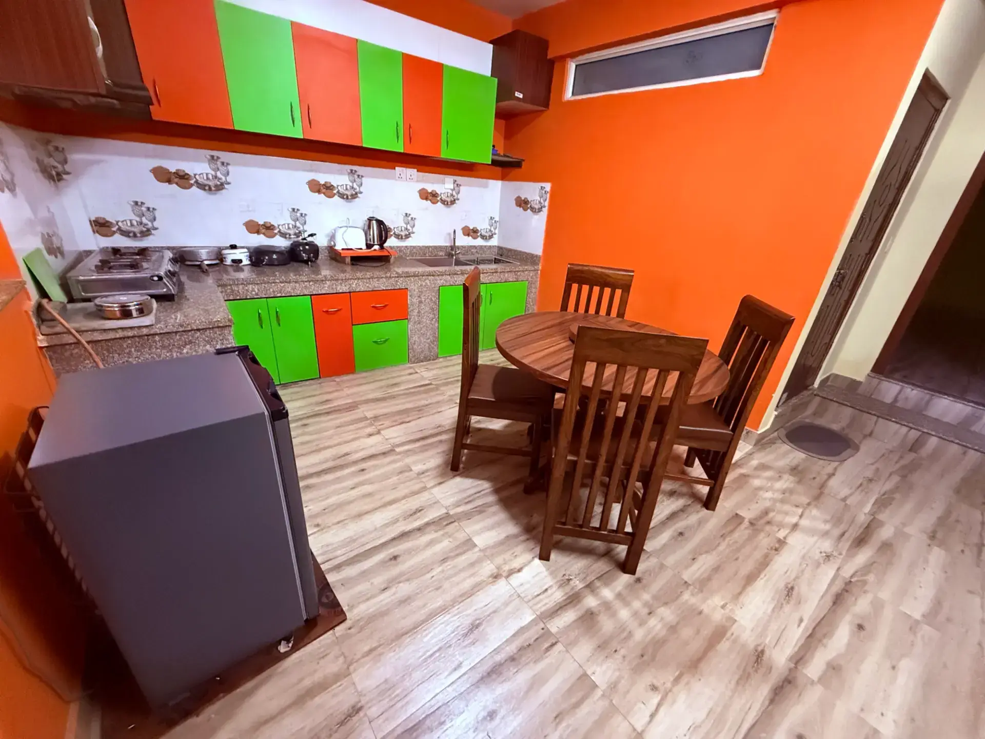 Bright orange-and-green apartment kitchen with fridge and dining set