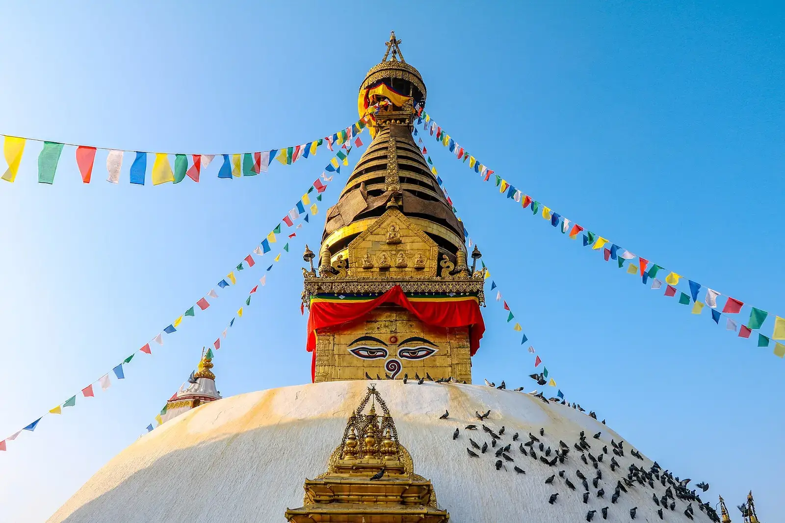 Swayambhunath Stupa with Buddha eyes, golden spire and prayer flags against a blue sky